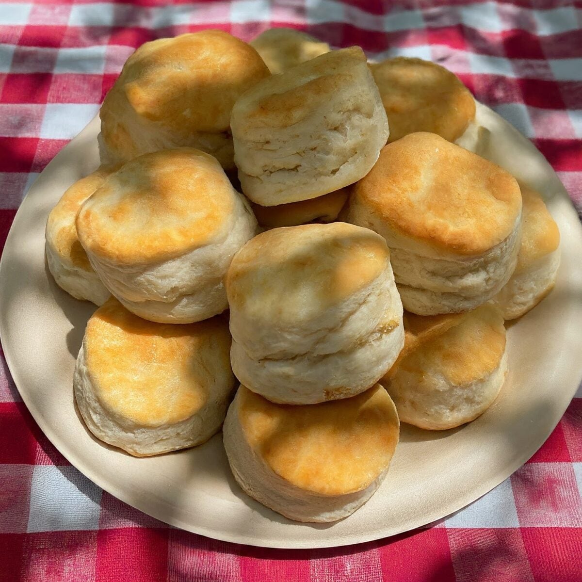 A plate of freshly baked, fluffy biscuits on a red and white checkered tablecloth.