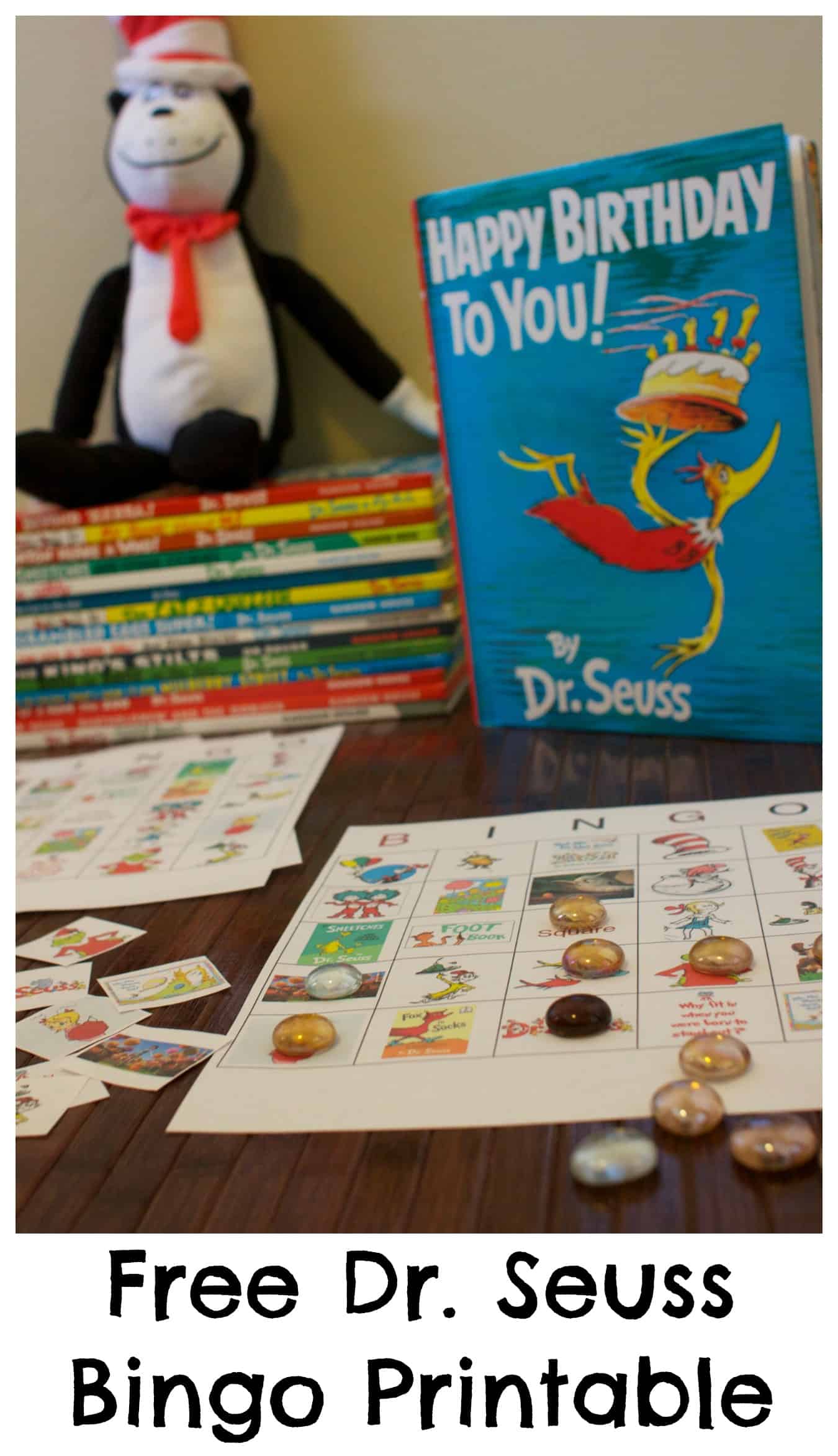 A Dr. Seuss-themed bingo game laid out on a table with a stack of books and a plush toy beside it, and text at the bottom saying "Dr. Seuss Bingo Game Free Printable
