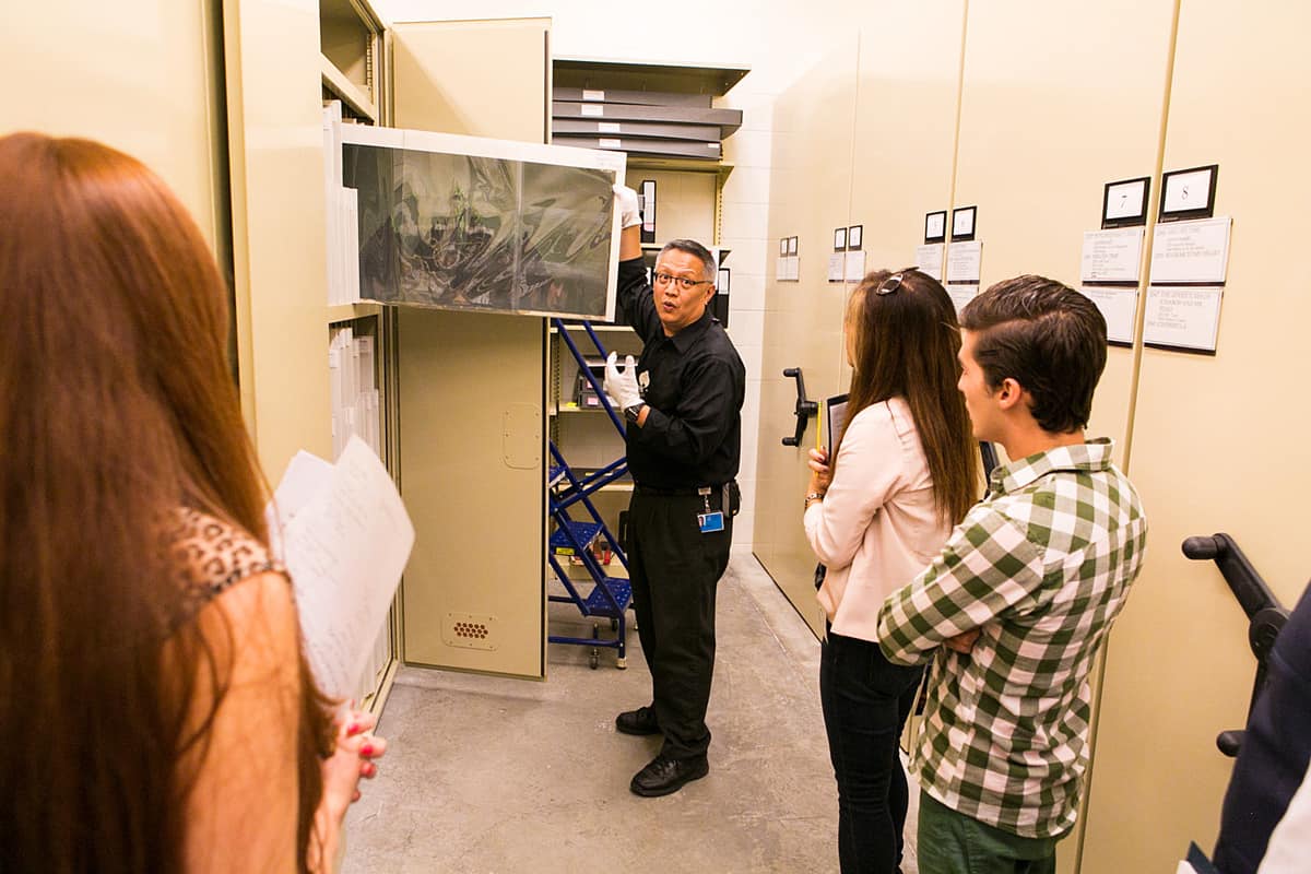 Tour guide showing visitors an art piece in storage at the Disney Animation Research Library.