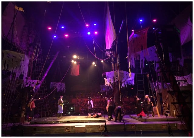 Rehearsal on a theater stage designed for Pirate's Dinner Adventure in Buena Park, with performers and crew preparing for a production under stage lighting.