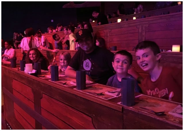 Audience members posing for a photo while seated at a dimly lit Pirate's Dinner Adventure show in Buena Park.