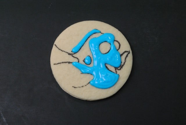 A cookie with blue icing designed to look like Finding Dory, featuring an abstract, artistic pattern on a black surface.