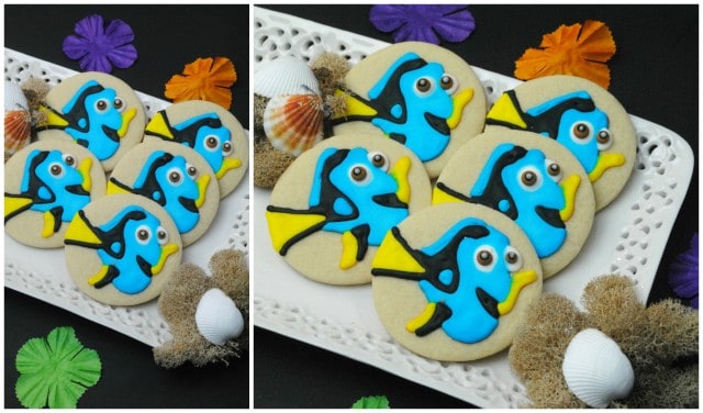 Decorated Finding Dory sugar cookies resembling tropical fish on a white plate with seashells and sea-themed decorations around it.
