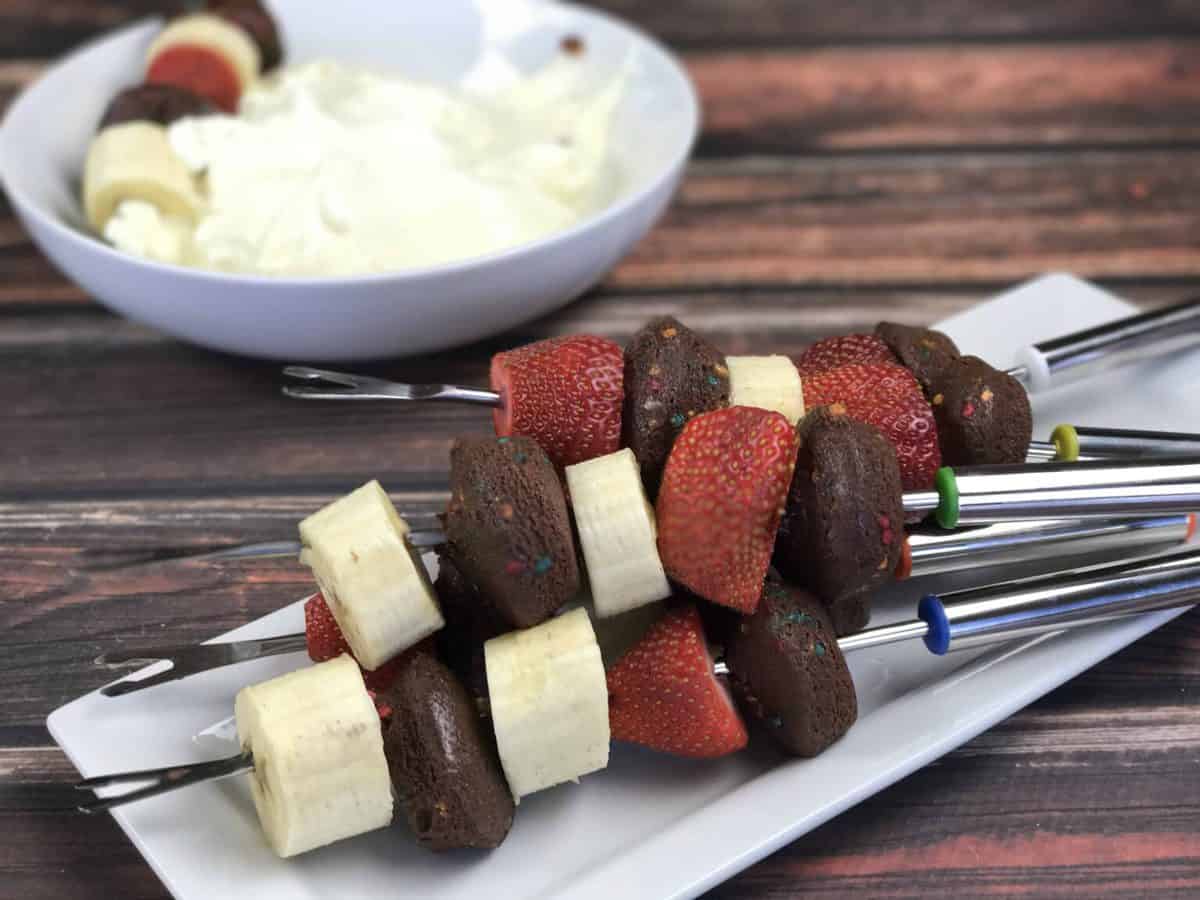 A plate of food on a wooden cutting board, with Cream cheese and Skewer