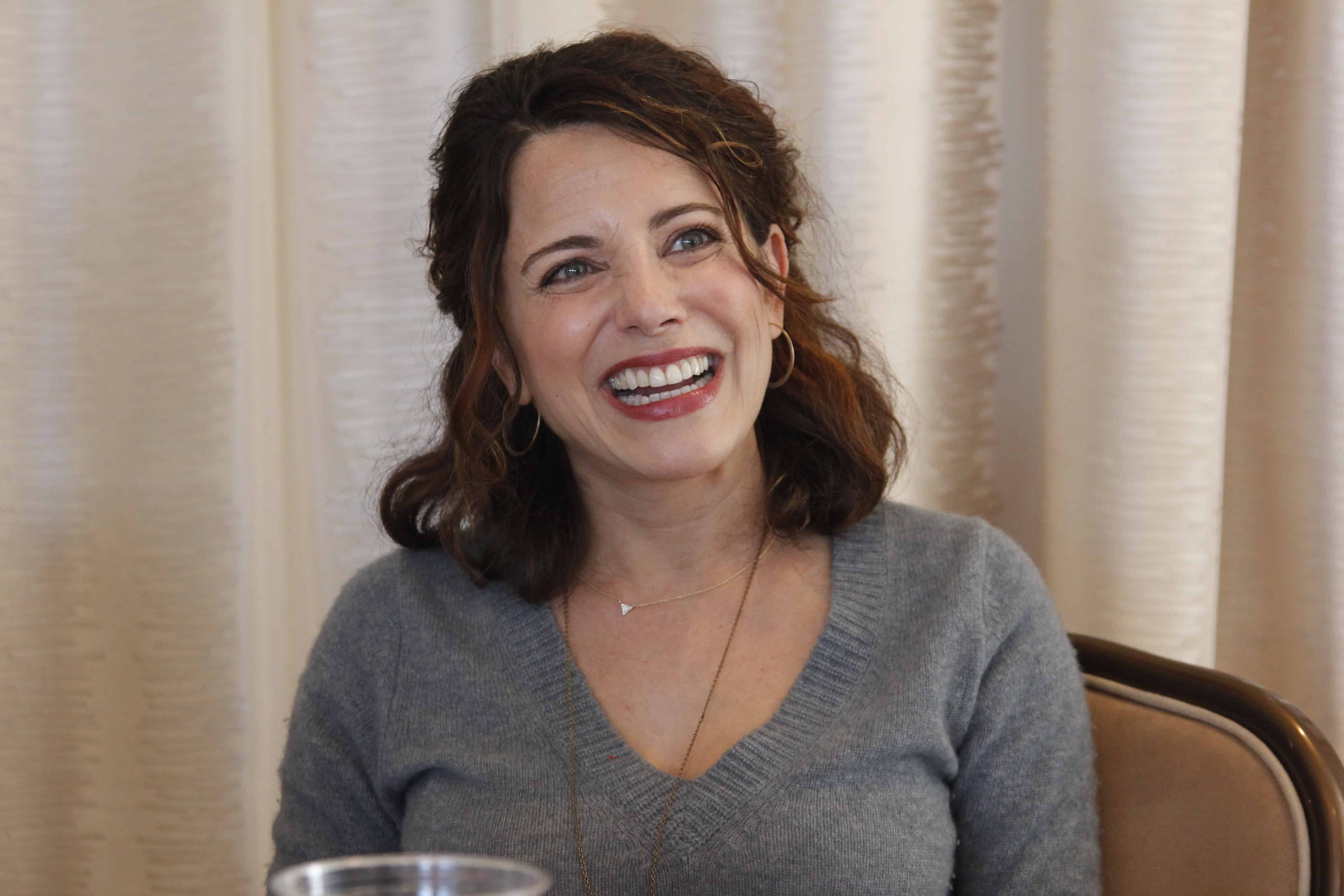 Alanna Ubach sitting at a table in front of a curtain