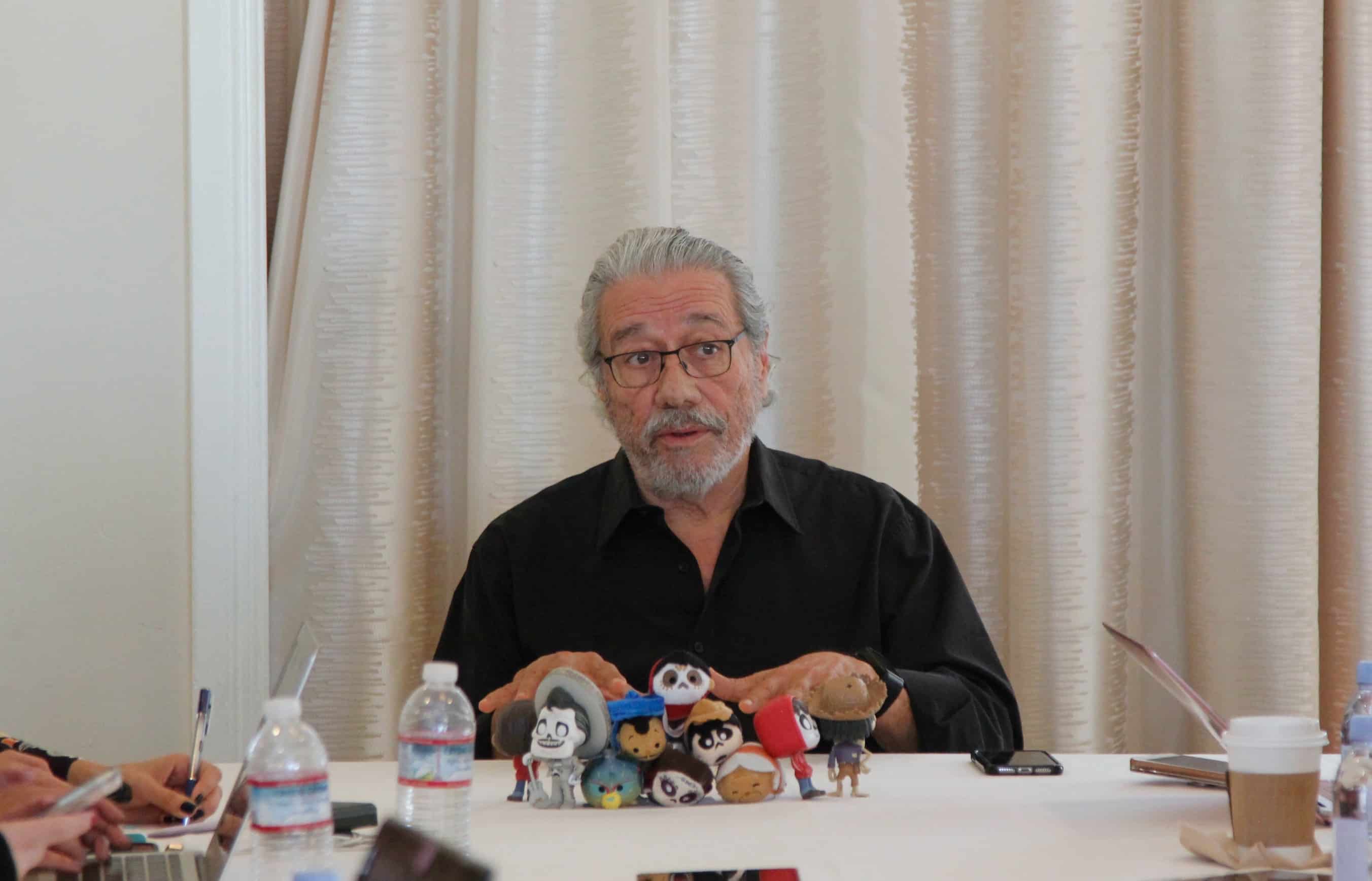 Edward James Olmos sitting at a table in front of a curtain