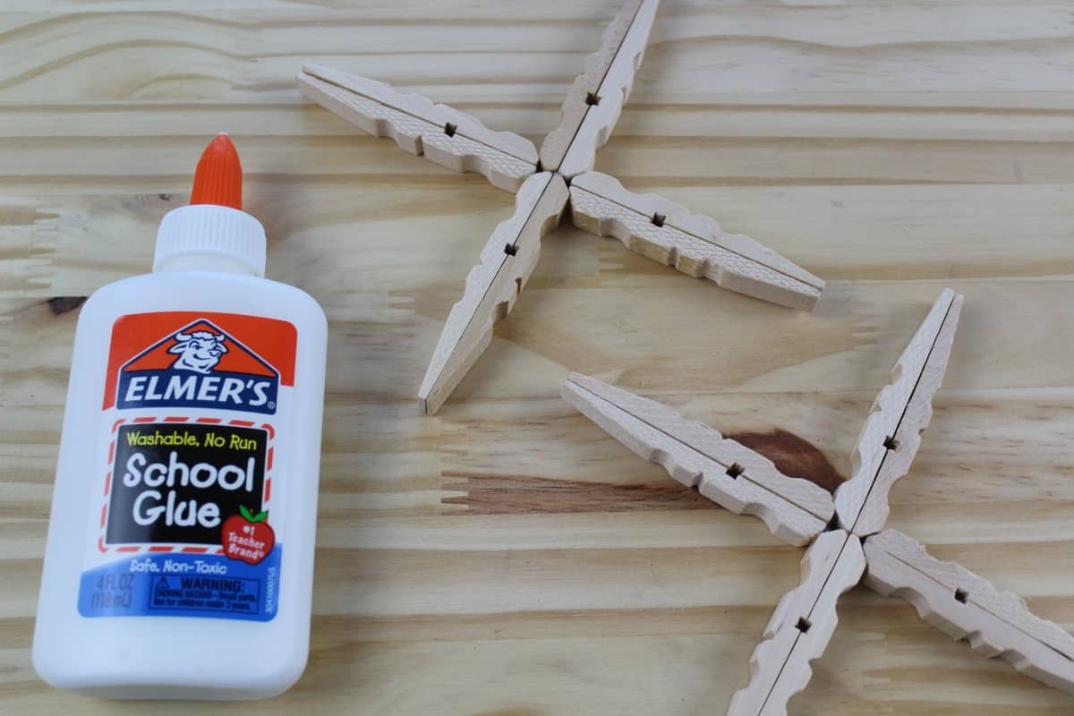 A knife sitting on top of a wooden cutting board, with Clothespin and Glitter Snowflake Ornaments