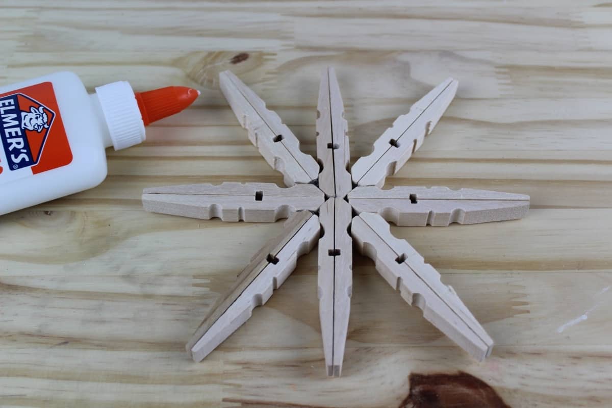 A knife sitting on top of a wooden cutting board, with Clothespin and Glitter Snowflake Ornaments