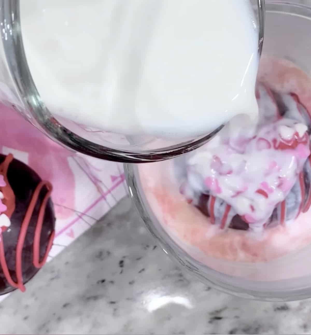 Pouring milk into a glass over a colorful hot cocoa bombs recipe.
