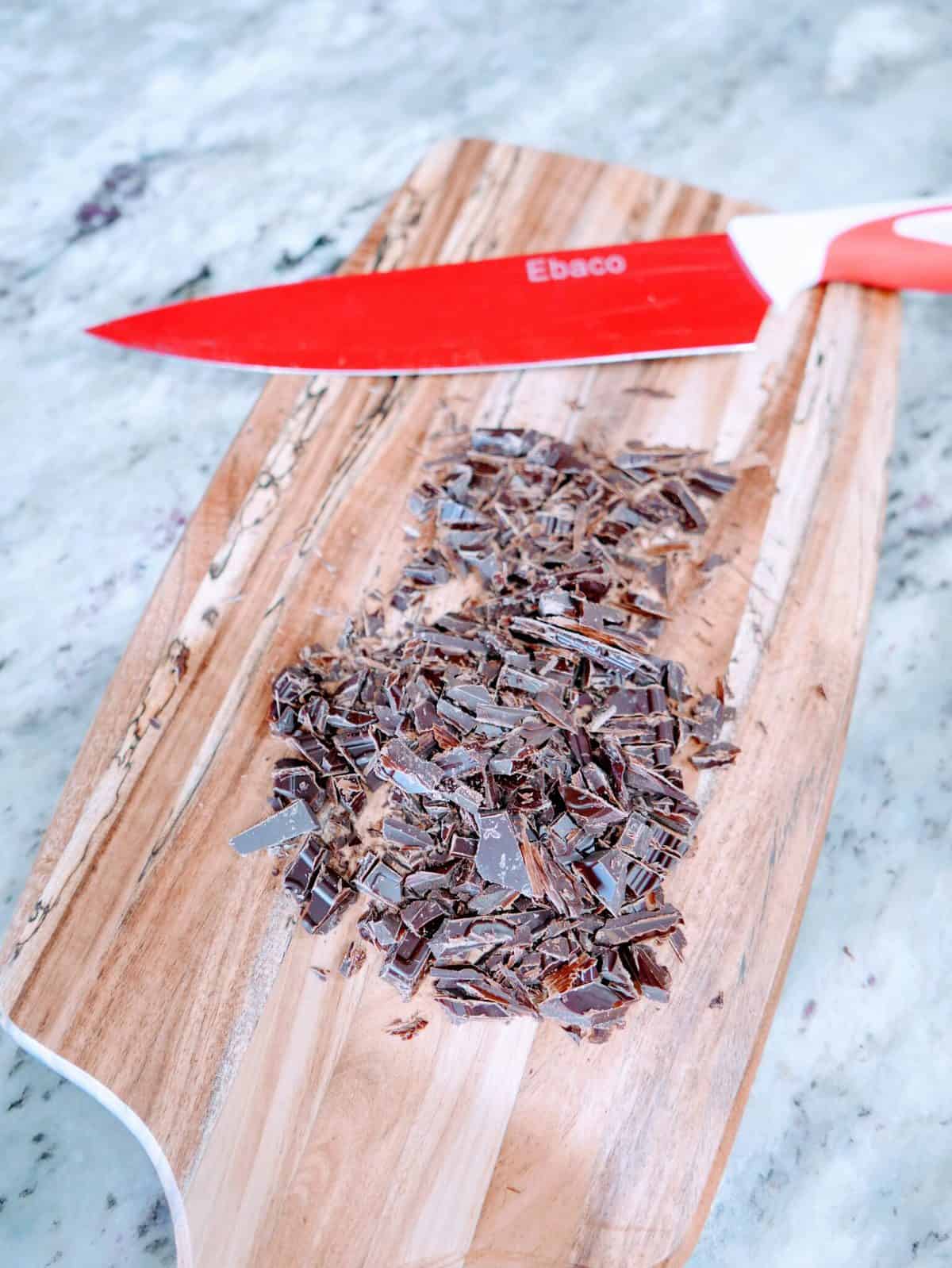 Finely chopped chocolate on a wooden cutting board with a red knife.