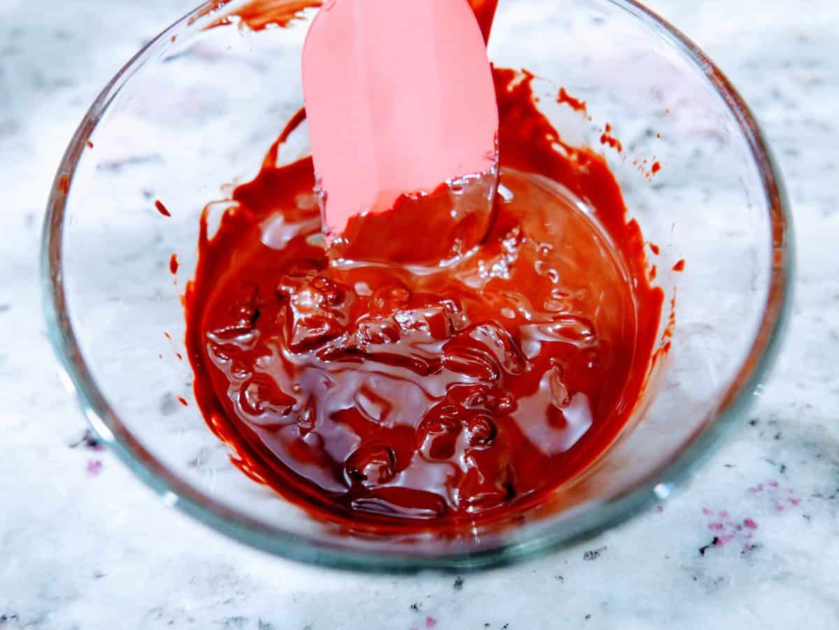 Mixing red food coloring or gelatin in a glass bowl with a spatula.