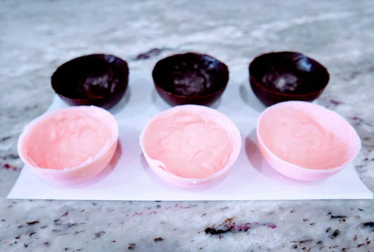 Three pink and two purple empty easter egg halves placed on a marble surface.