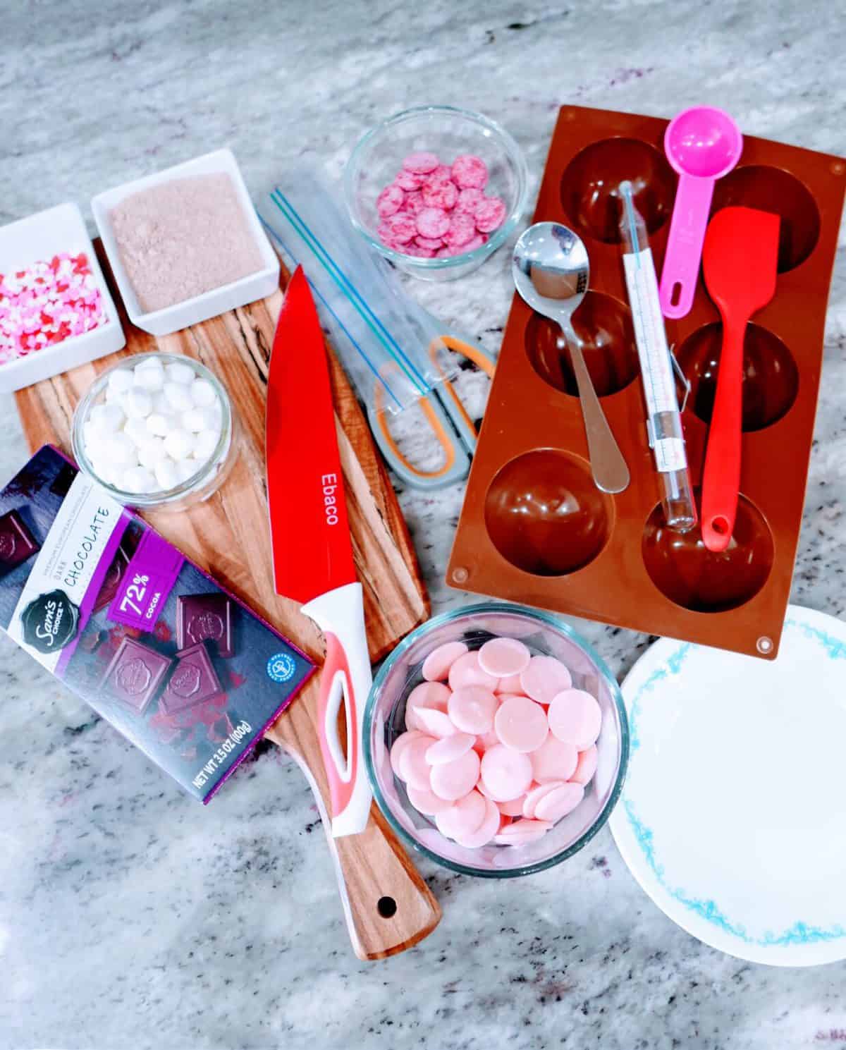 Assorted baking tools and ingredients, including chocolate molds, sprinkles, and melting wafers, arranged on a kitchen counter.