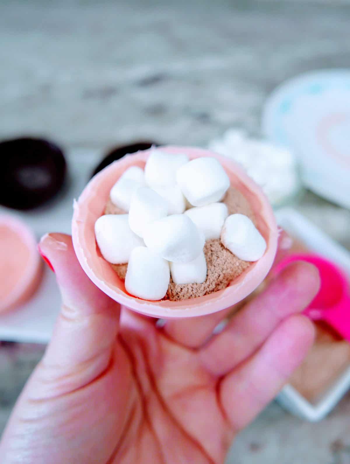A hand holding a chocolate-filled easter egg topped with marshmallows.
