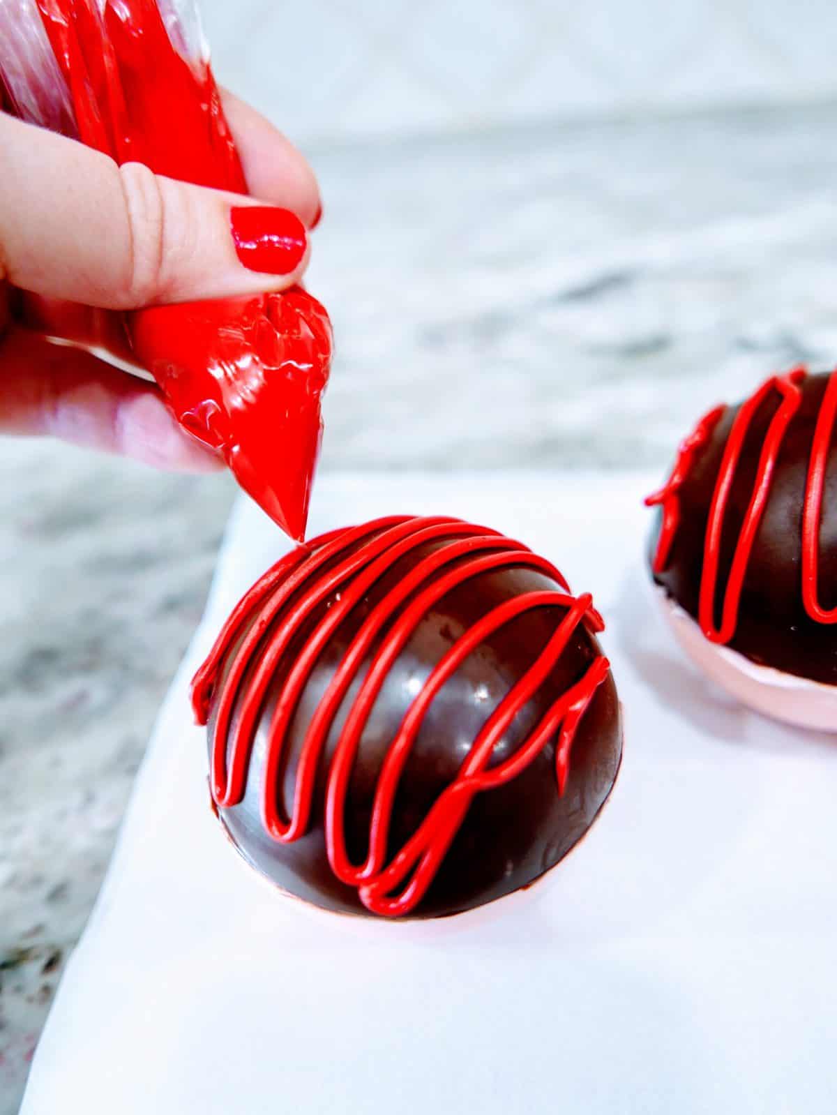 Decorating chocolate truffles with red icing.