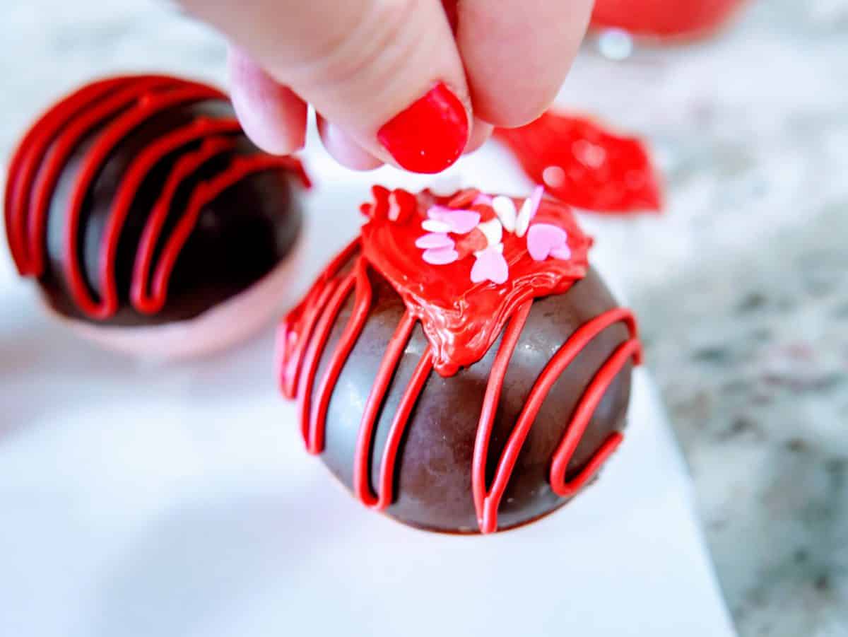 Decorating a chocolate ball with red icing and small pink sprinkles.