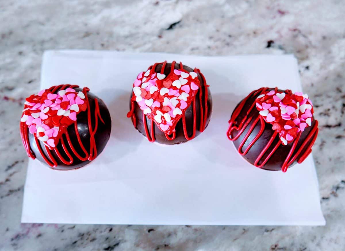 Three decorated cupcakes with heart sprinkles displayed on a plate.