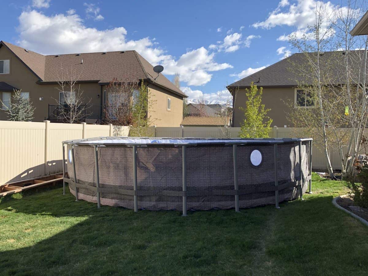 Above ground swimming pool in a residential backyard with houses and a clear sky in the background.
