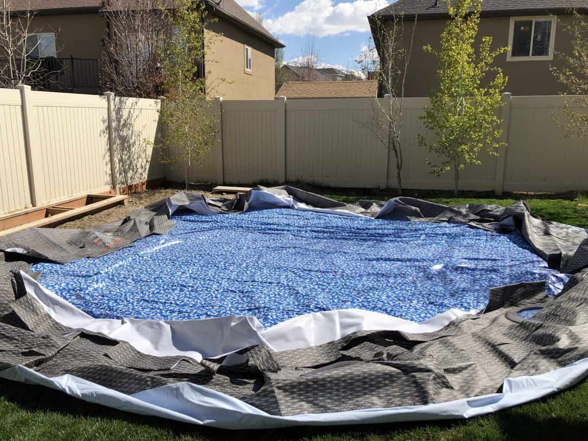 A partially assembled above-ground pool with a blue cover, surrounded by a neat yard and a white fence.