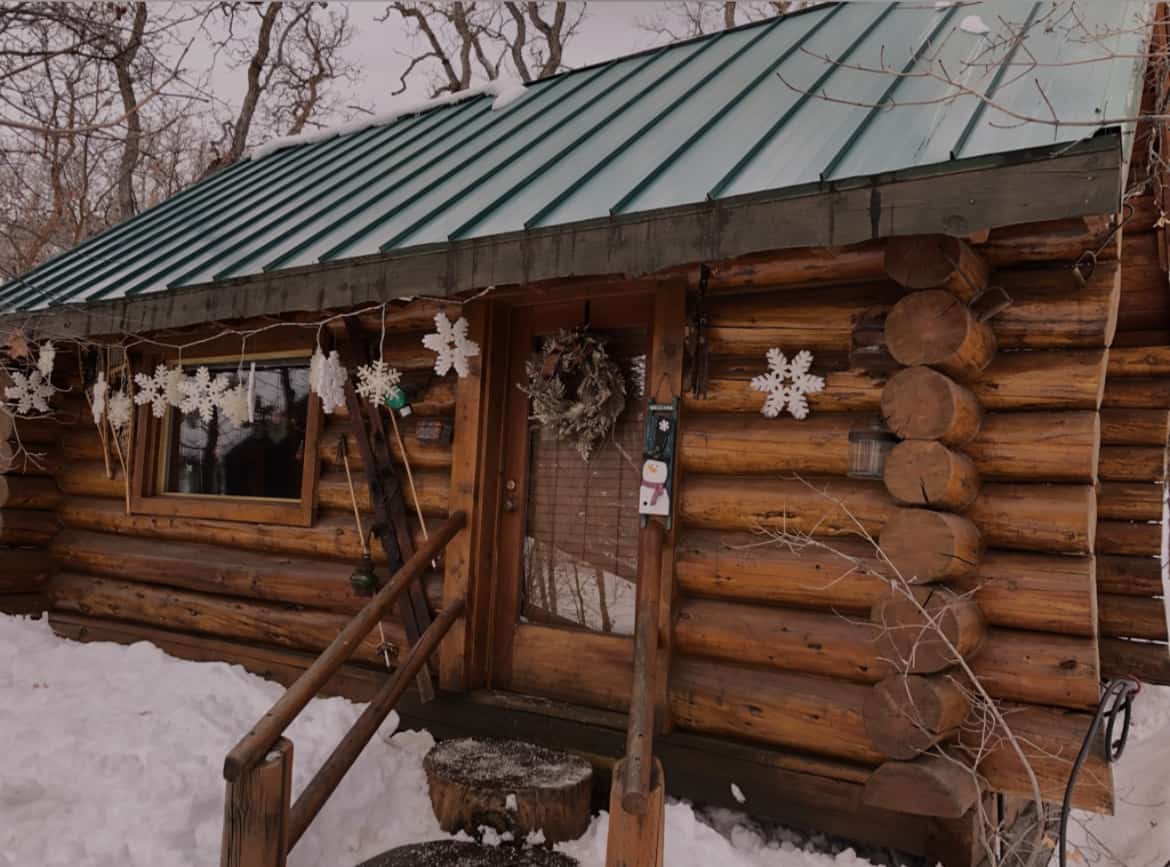 Snowflake decorations adorn a wooden cabin in a snowy setting, next to a homemade hot chocolate recipe resting on the kitchen counter.