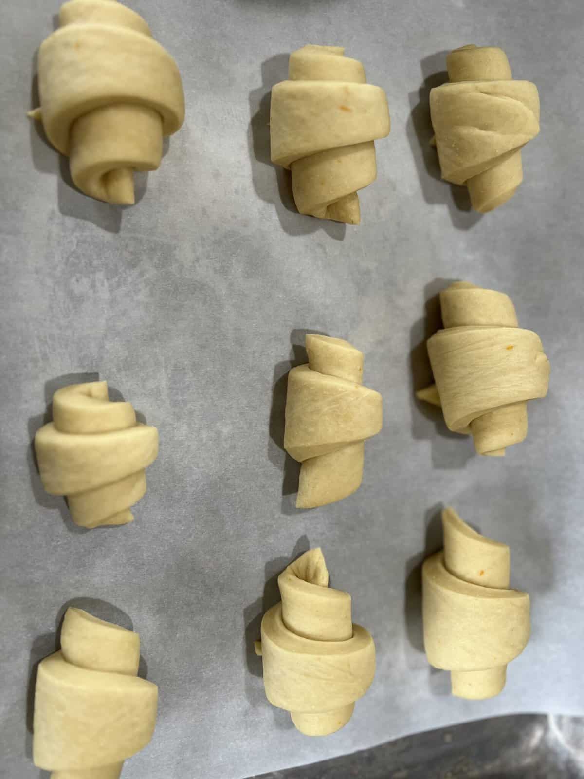 Unbaked orange rolls arranged on a baking sheet lined with parchment paper.