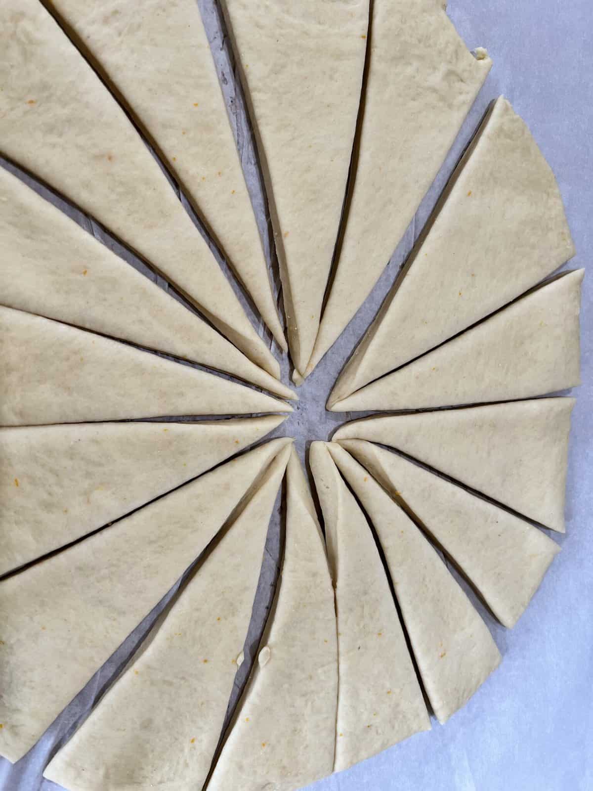 Unbaked orange rolls dough cut into triangular shapes on parchment paper.