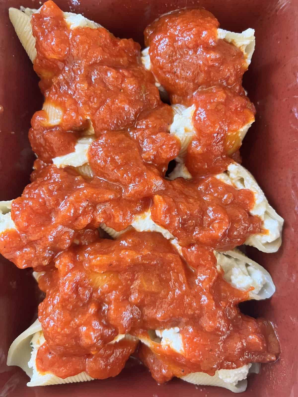 A delicious and comforting serving of stuffed shells in a red baking dish. The jumbo pasta shells are filled with a creamy mixture of ricotta cheese, Parmesan cheese, and herbs, then baked in a rich tomato sauce until hot and bubbly. The red baking dish adds a pop of color and makes for a beautiful presentation. This classic Italian dish is perfect for serving at a family gathering or enjoying as a cozy weeknight dinner.