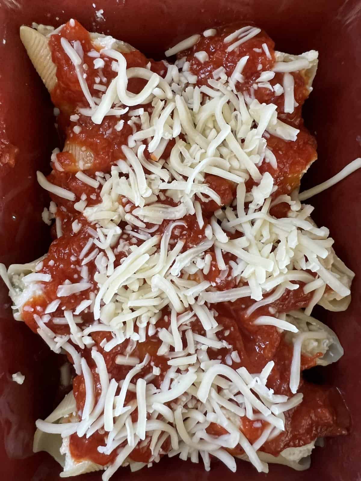 A delicious and comforting serving of stuffed shells in a red baking dish. The jumbo pasta shells are filled with a creamy mixture of ricotta cheese, Parmesan cheese, and herbs, then baked in a rich tomato sauce until hot and bubbly. The red baking dish adds a pop of color and makes for a beautiful presentation. This classic Italian dish is perfect for serving at a family gathering or enjoying as a cozy weeknight dinner.
