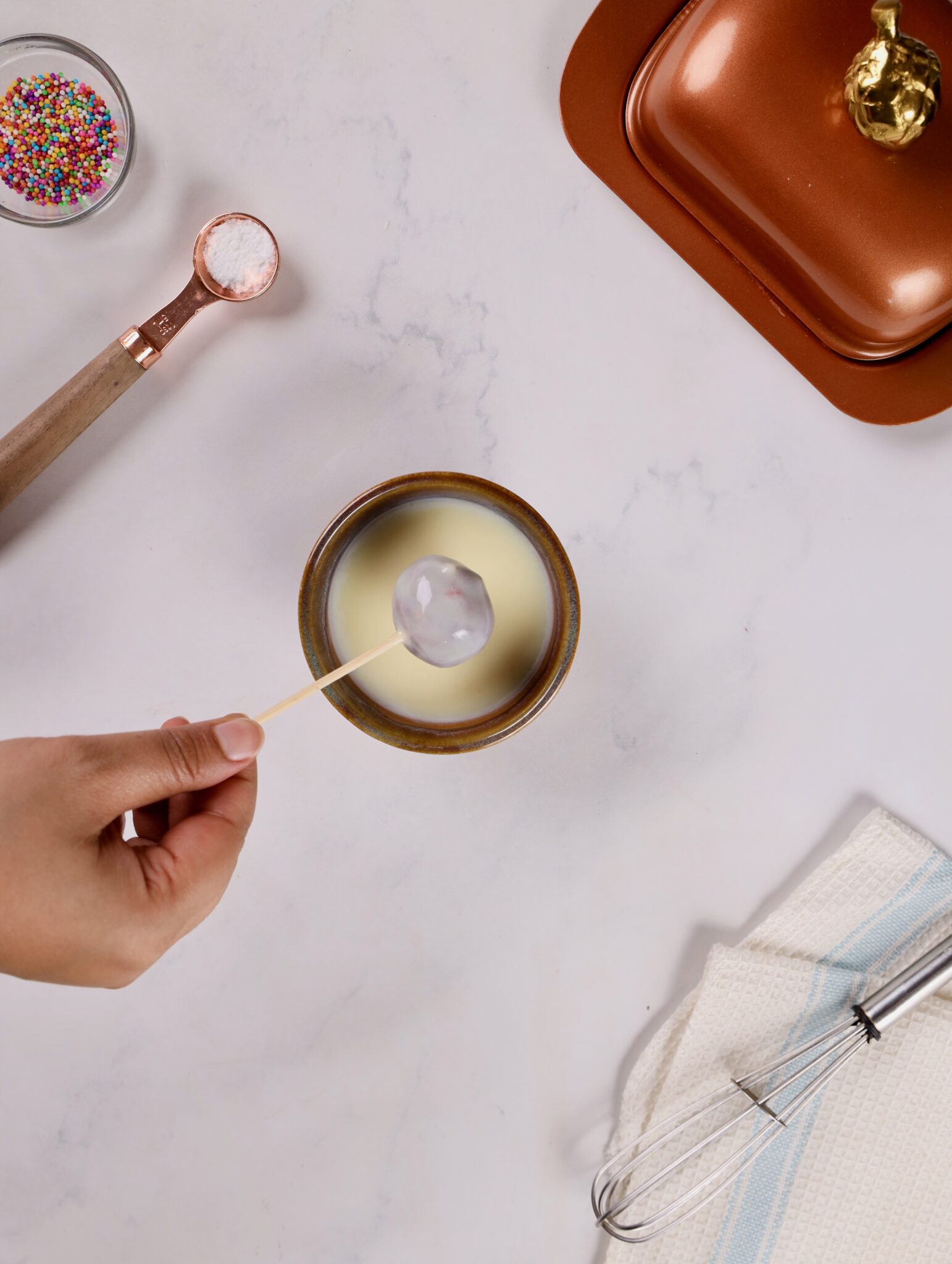 Submerging a cake ball into a bowl of smooth, melted white chocolate.