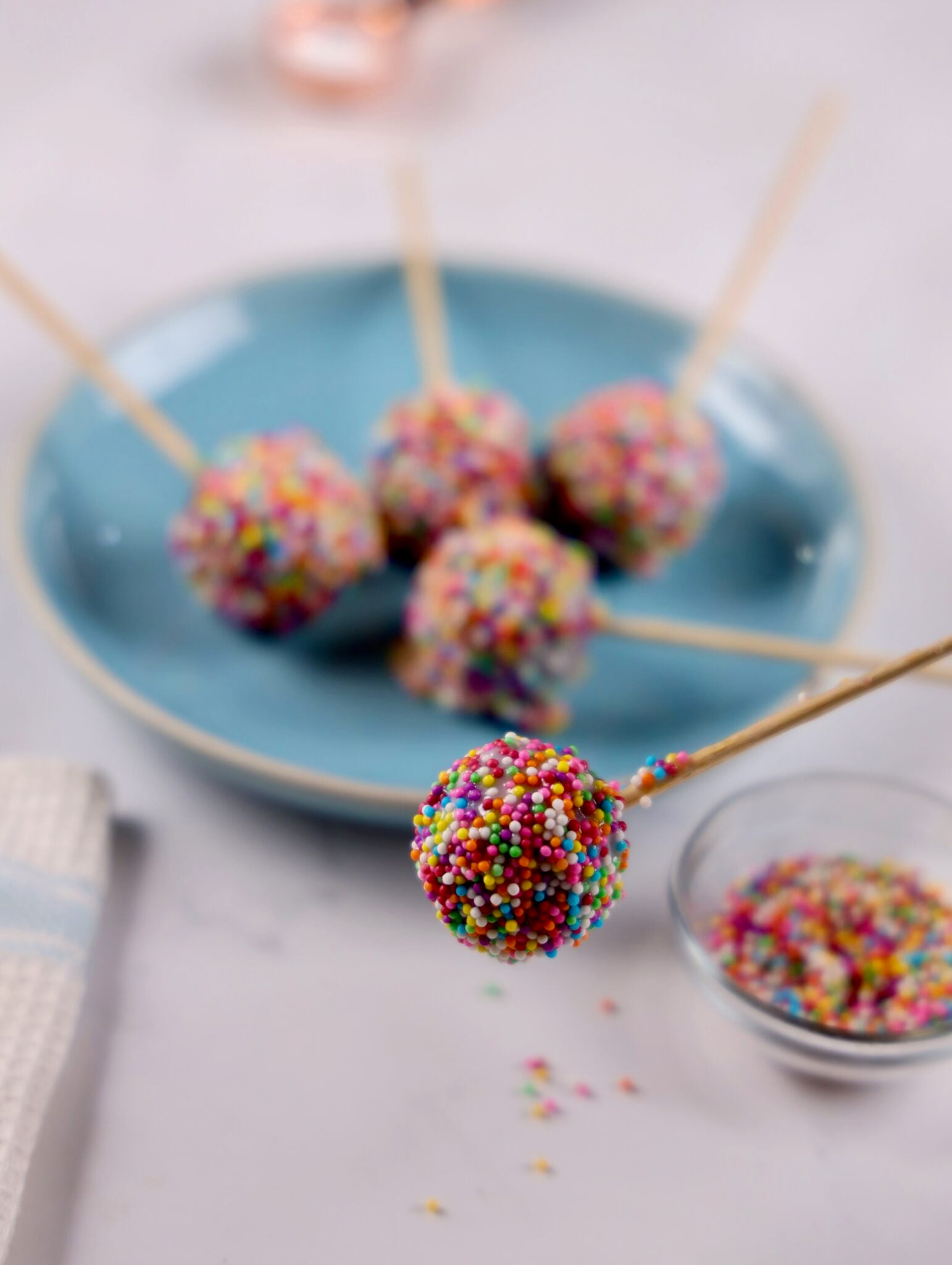 A blue plate of finished red velvet cake pops, glistening with white chocolate and sprinkles.