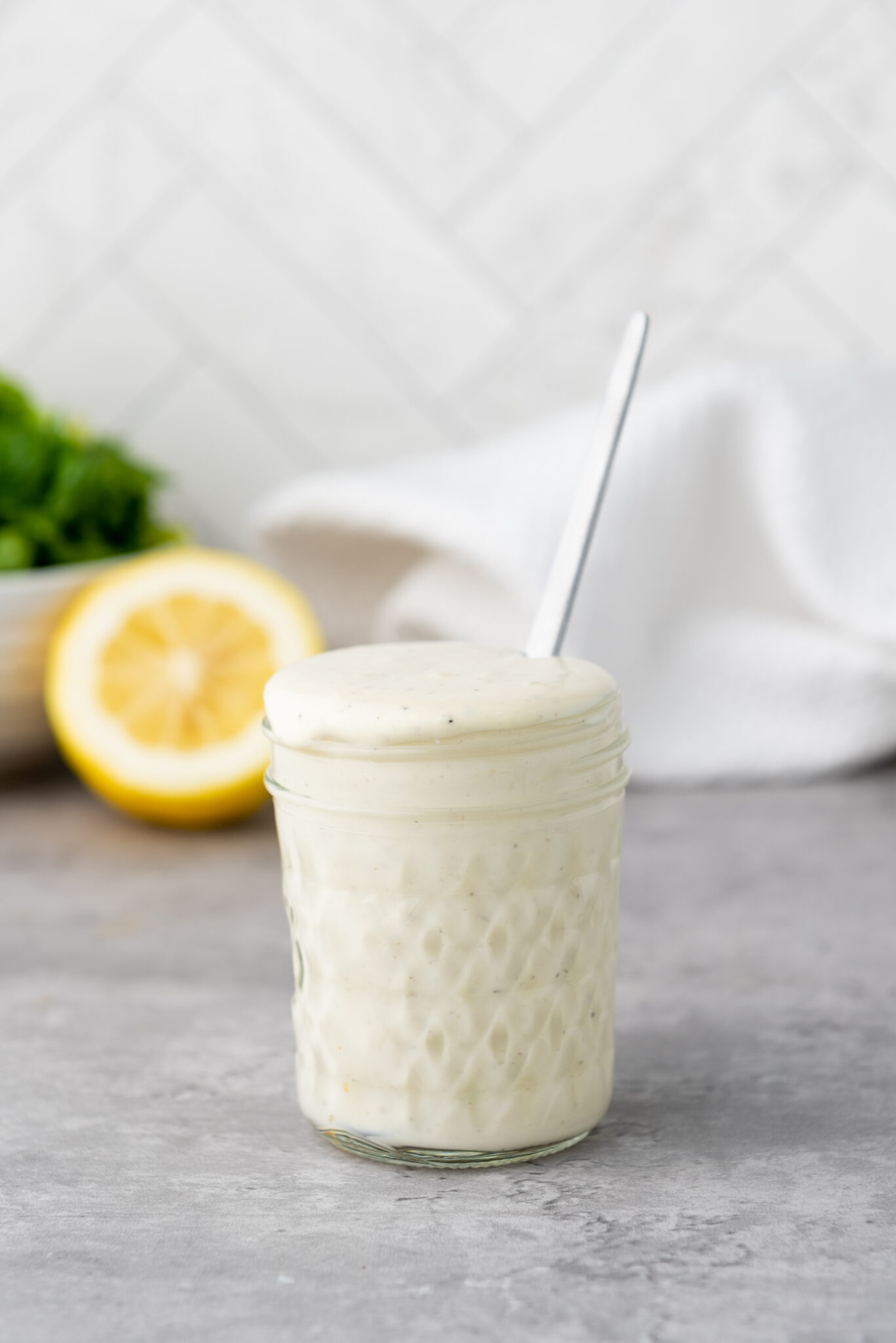 A transparent glass jar filled with freshly made creamy Caesar salad dressing, set against a rustic kitchen backdrop