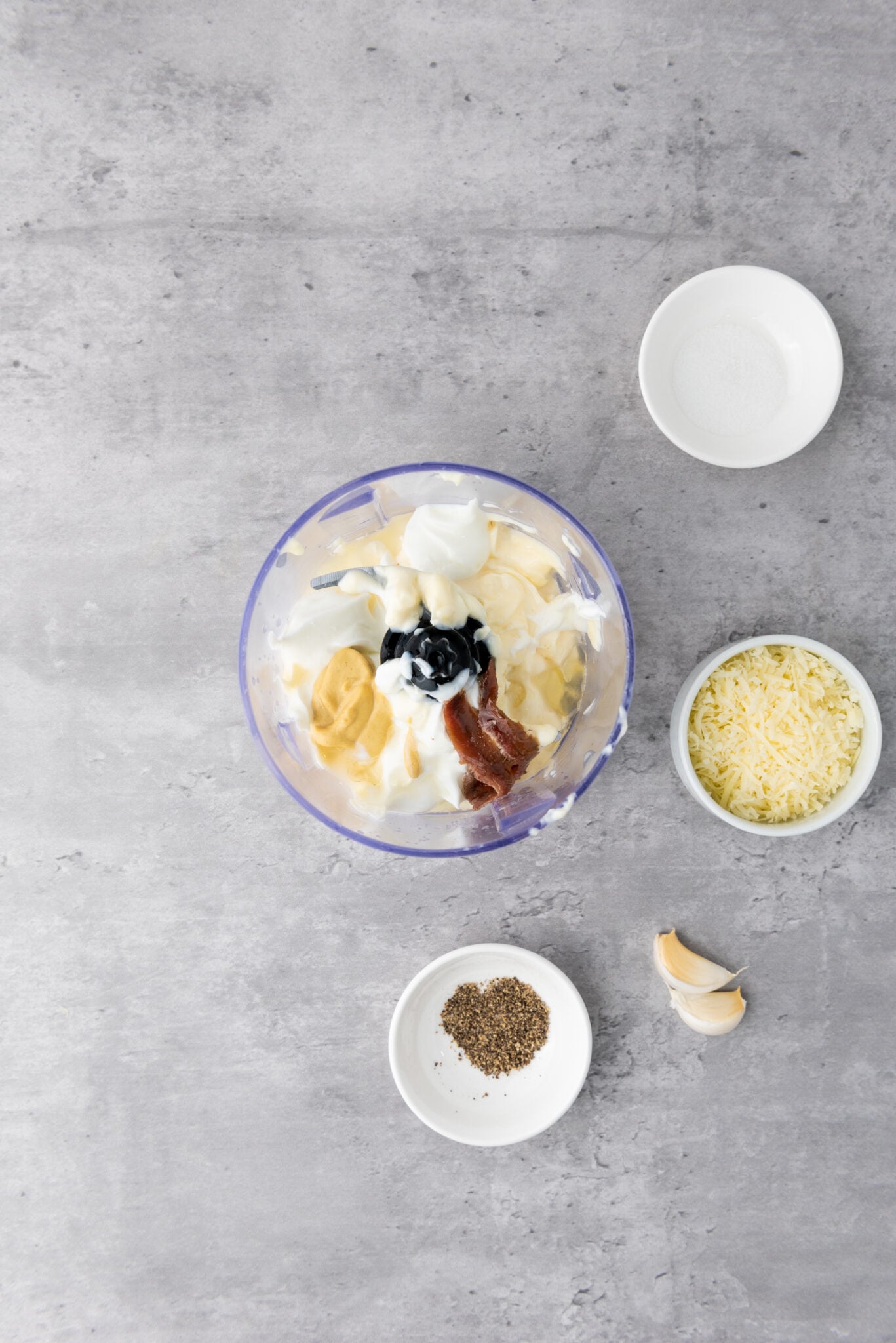 Two anchovies and a spoon of their oil being introduced to the mix, showcasing their distinct texture.