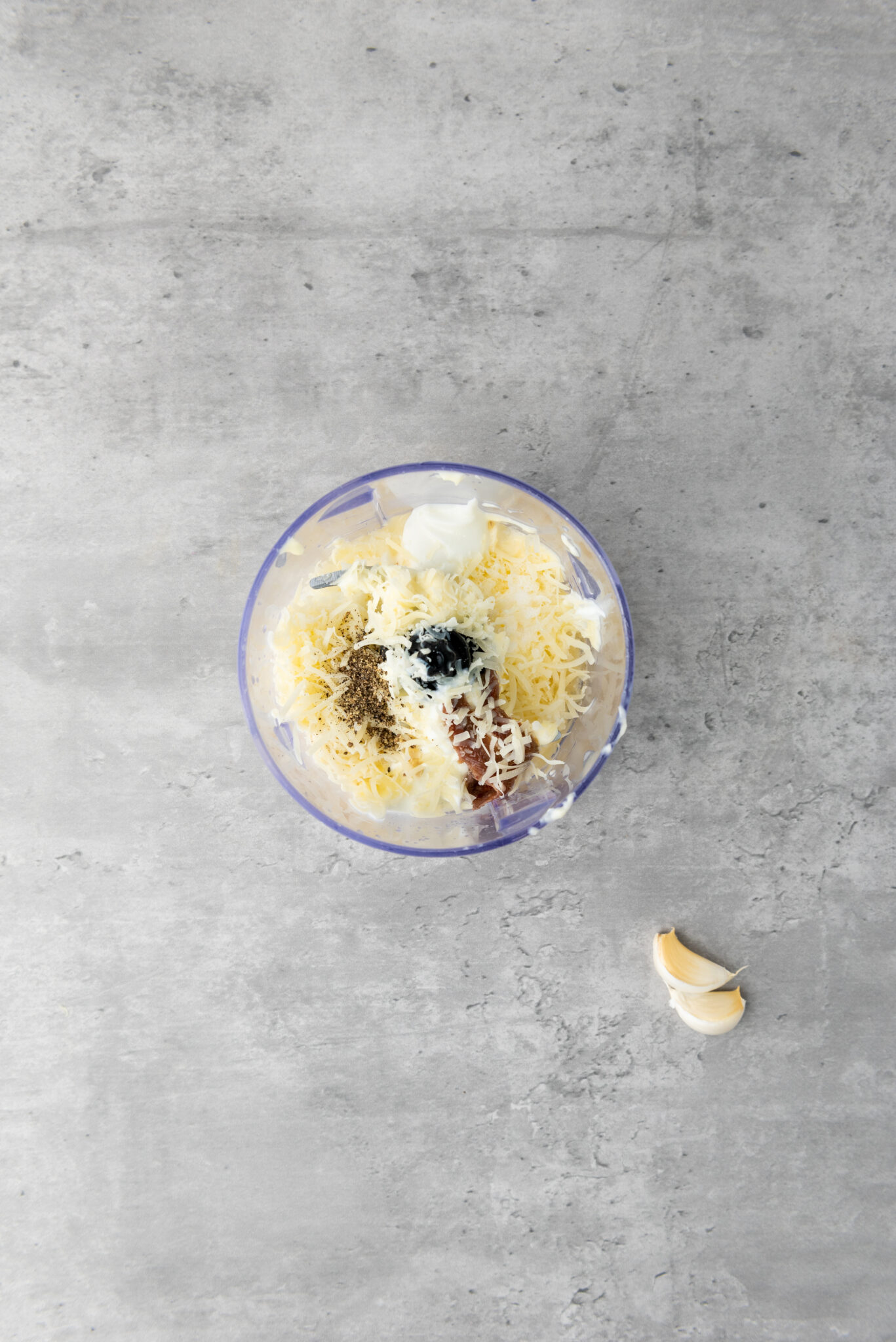 A teaspoon of Dijon mustard being spooned into the processor, its rich hue contrasting the lighter ingredients.