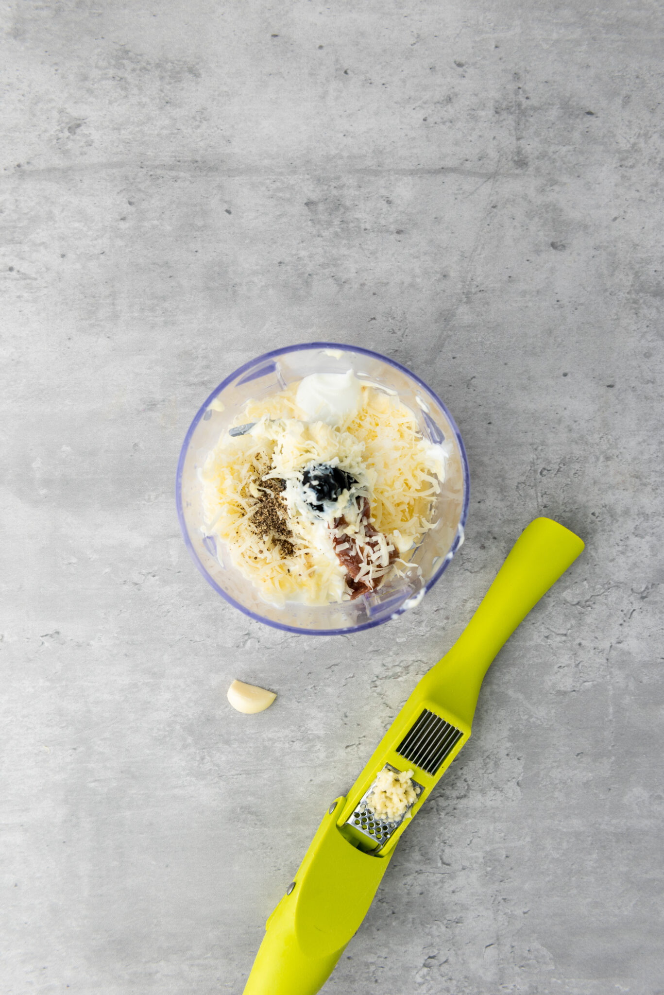 Sprinkling salt and black pepper, creating a fine mist above the accumulated ingredients in the processor.