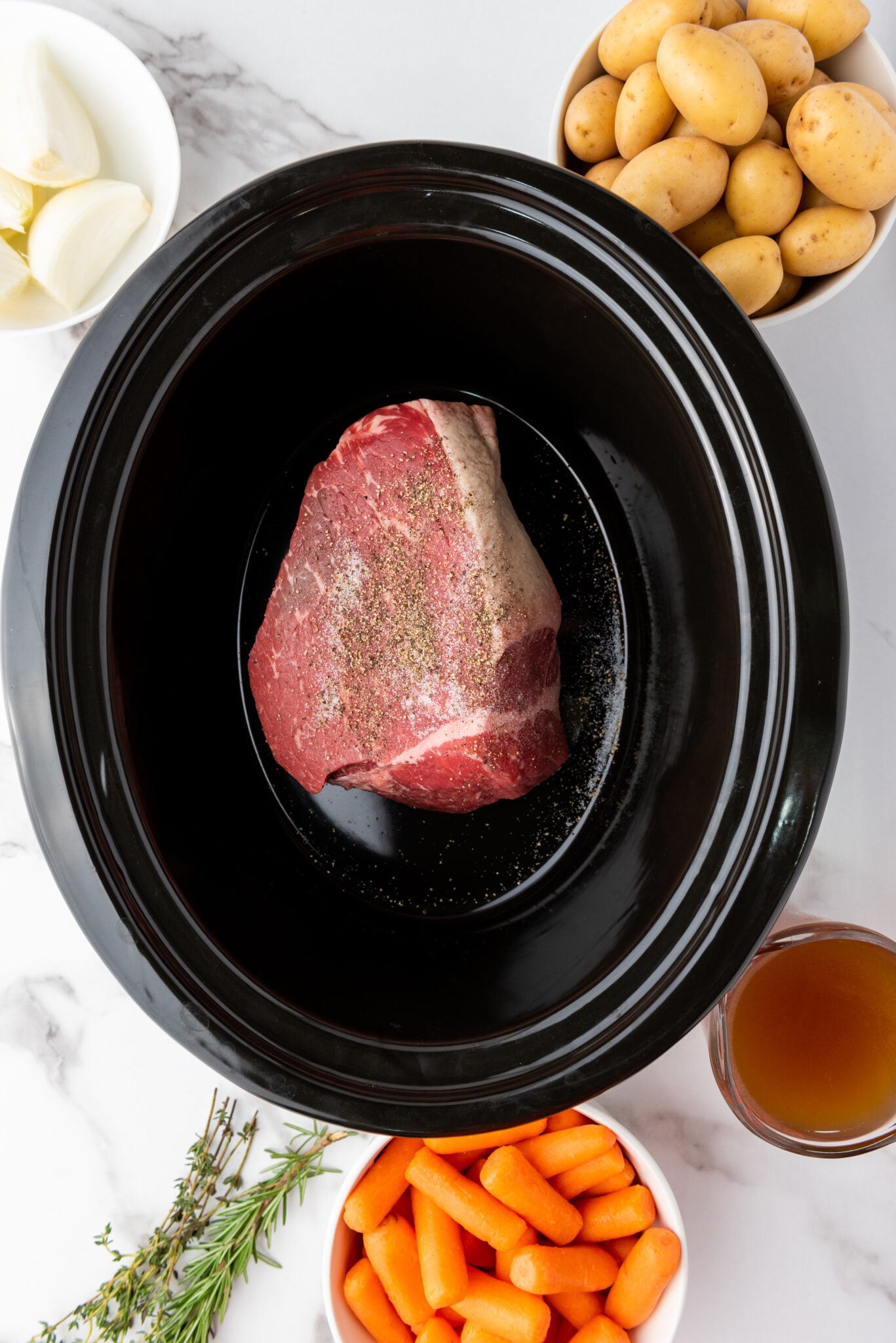 Seasoned rump roast placed neatly at the base of a slow cooker with salt and pepper added.