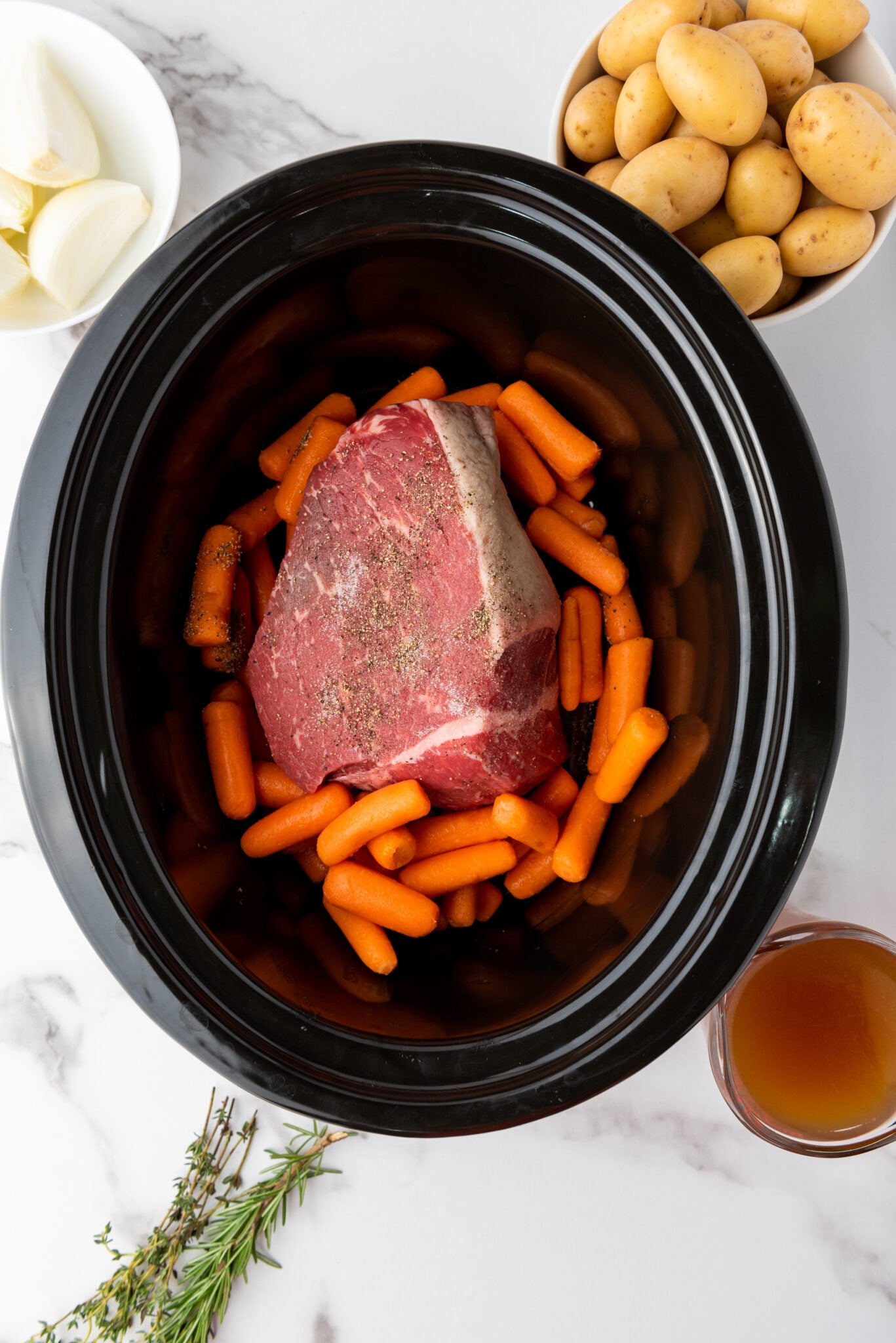 Slow cooker with layer of carrots around the rump roast.