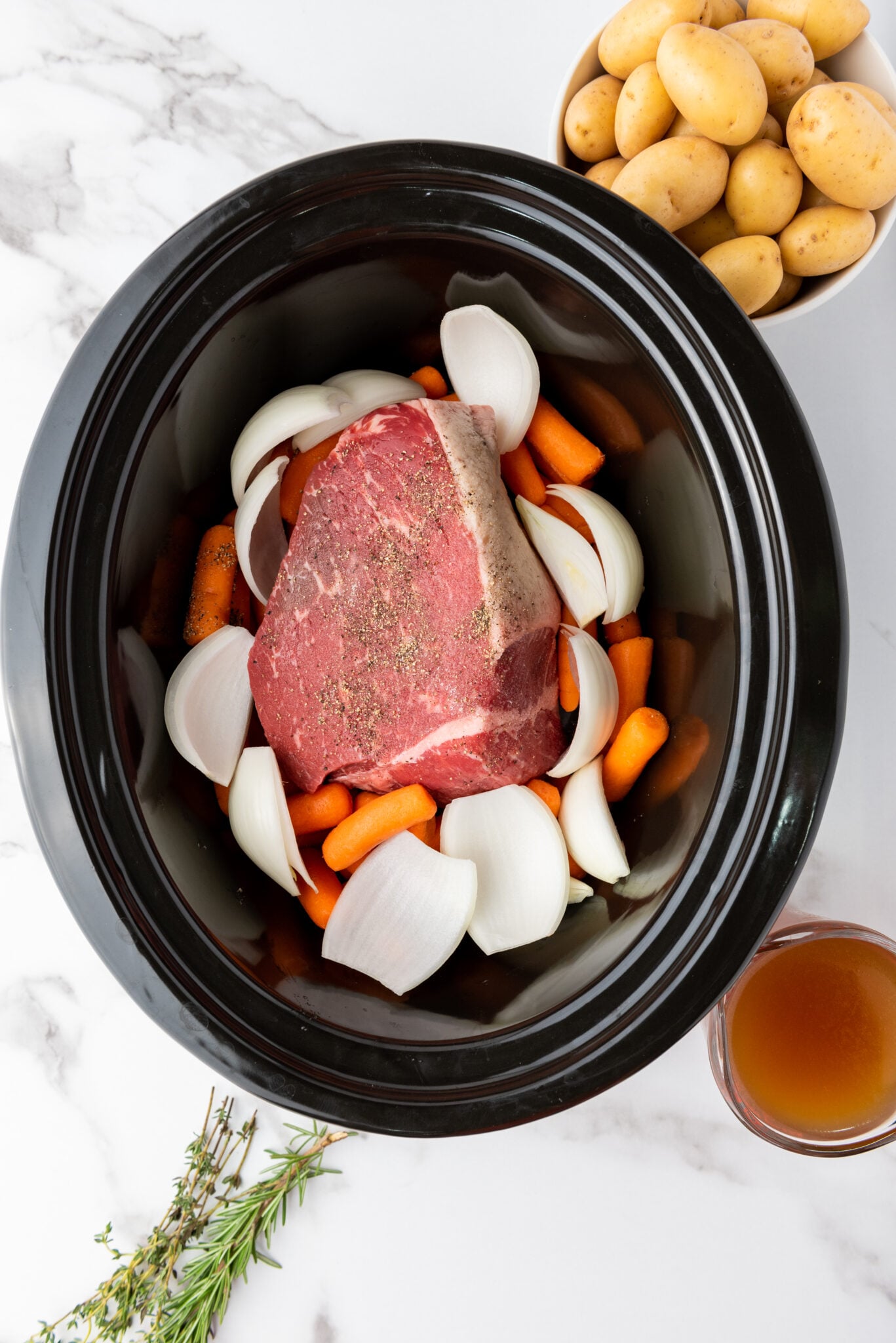 Slow cooker with layers of carrots, and onions around the rump roast.