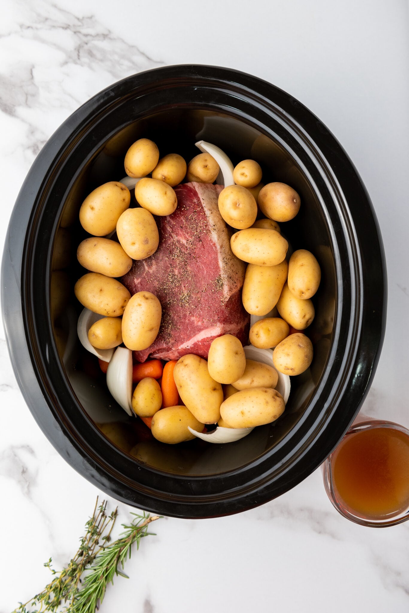 Slow cooker with layers of baby potatoes, carrots, and onions around the rump roast.