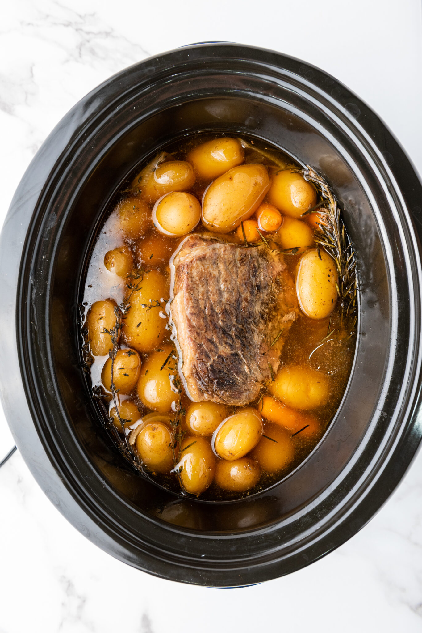 Mid-cooking peek inside the slow cooker showing the roast turning a deep brown.
