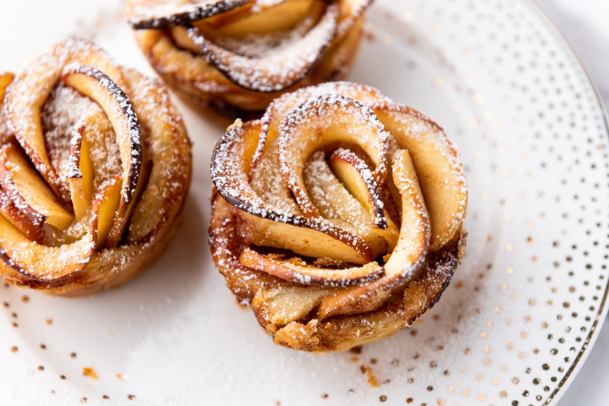Lush baked apple roses baked to perfection, their golden edges glistening, presented on a plate with soft ambient lighting accentuating their details.