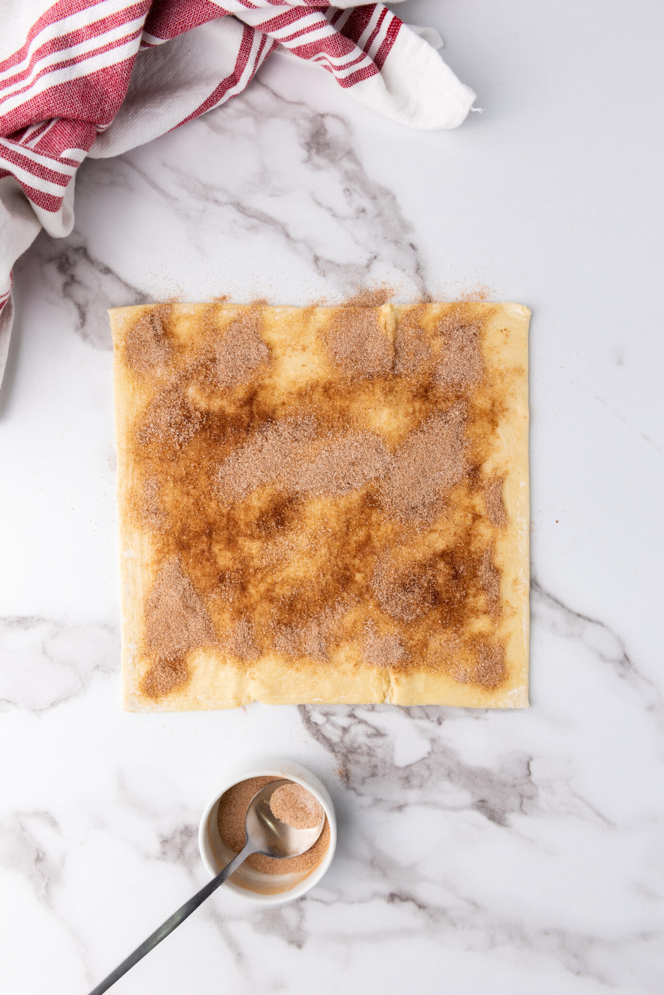 A sprinkle of cinnamon-sugar mix over a butter-glistened puff pastry sheet.