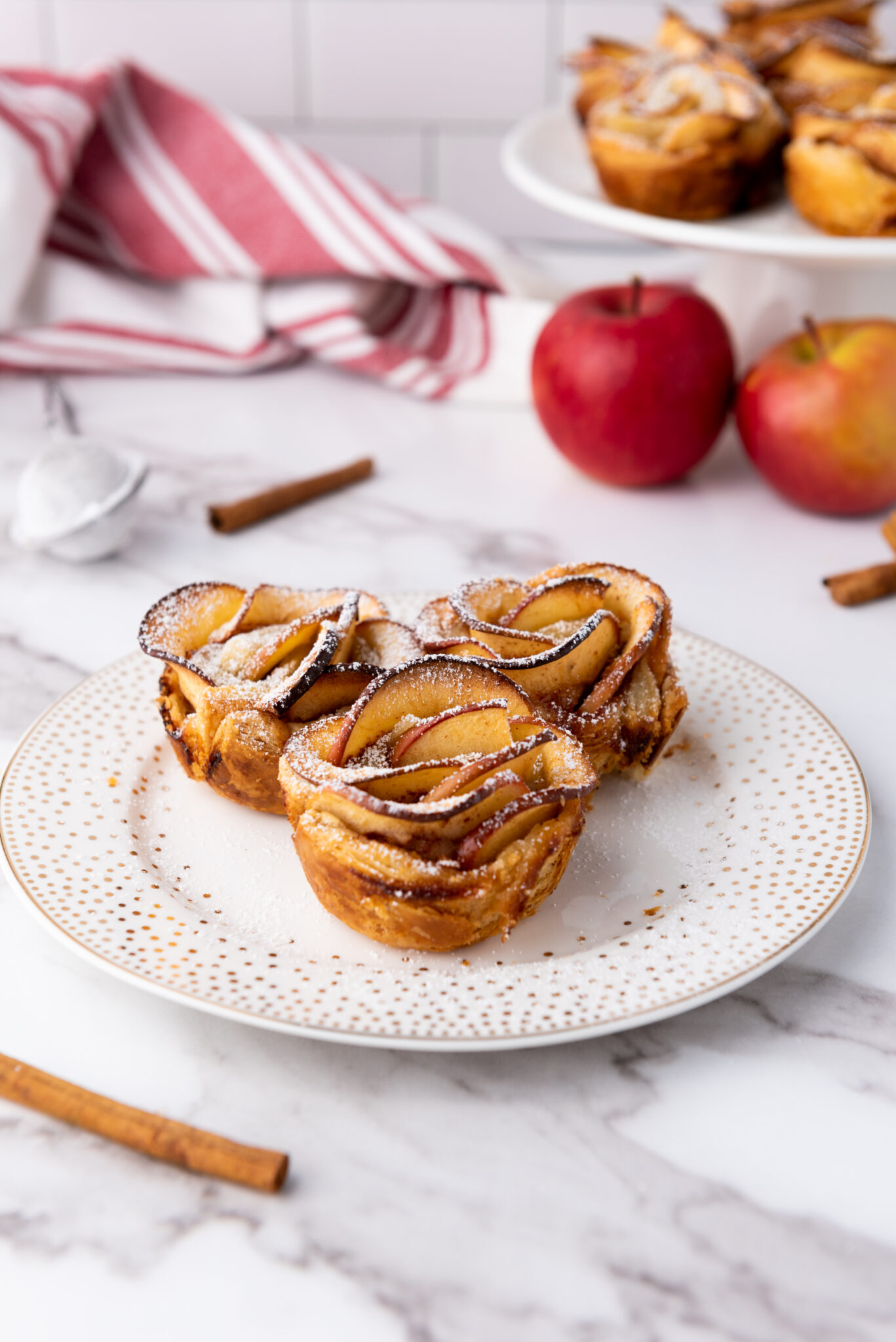 Lush apple roses baked to perfection, their golden edges glistening, presented on a plate with soft ambient lighting accentuating their details.