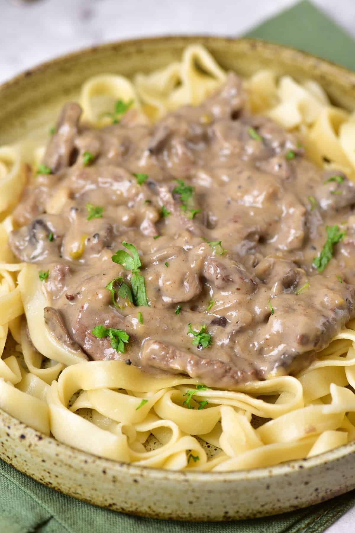 A plate of beef stroganoff served over egg noodles, garnished with parsley.