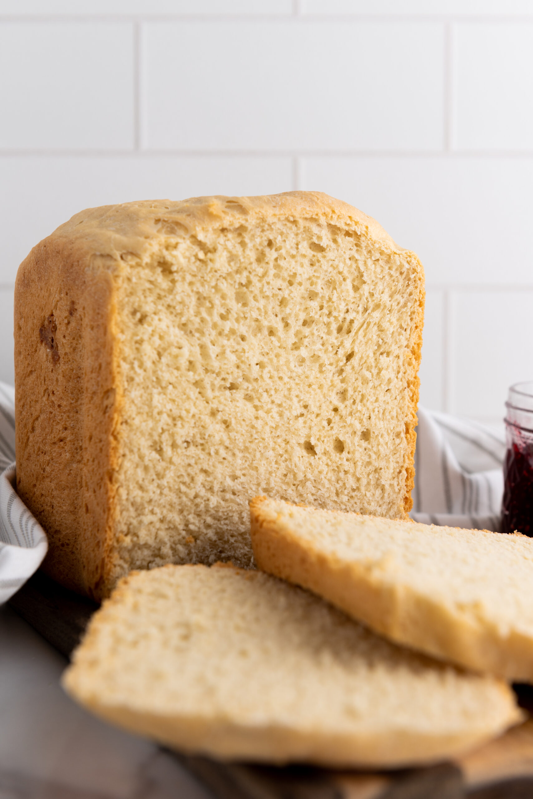 Close-up of a freshly cut white bread loaf, highlighting its soft, airy texture, placed beside a jar of jam.