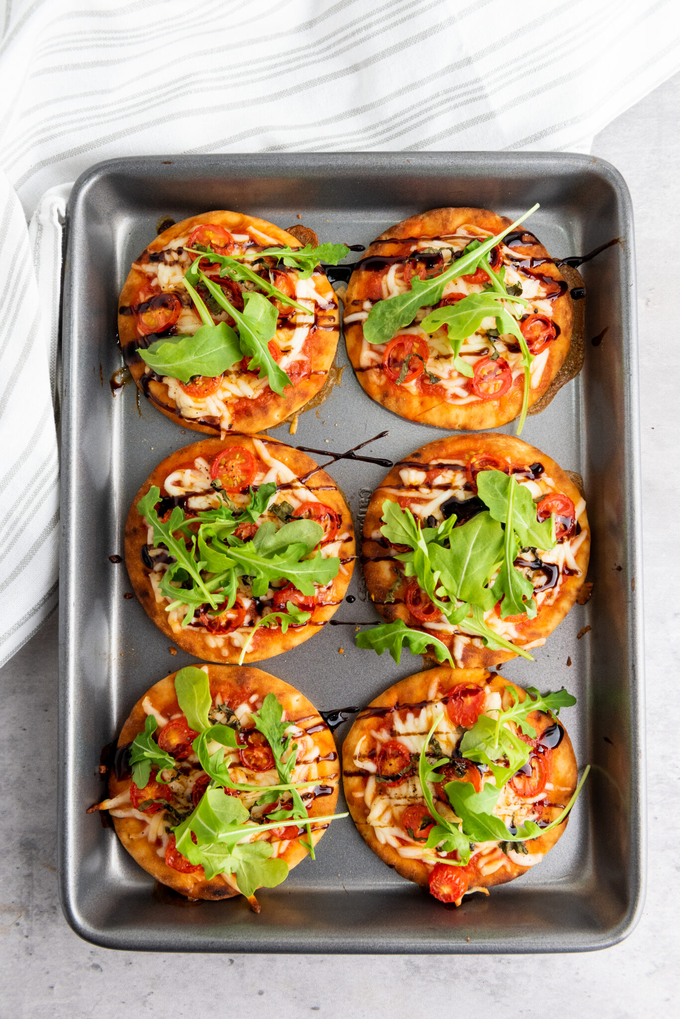 Freshly baked caprese pizza recipe drizzled with balsamic vinegar and arugula.