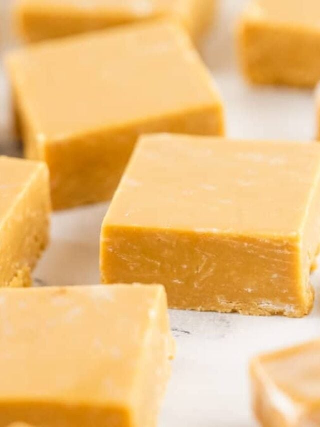 Close-up of several square pieces of light brown fudge arranged on a white surface. The fudge has a smooth texture with slightly visible ridges, reminiscent of an old-fashioned caramel recipe.