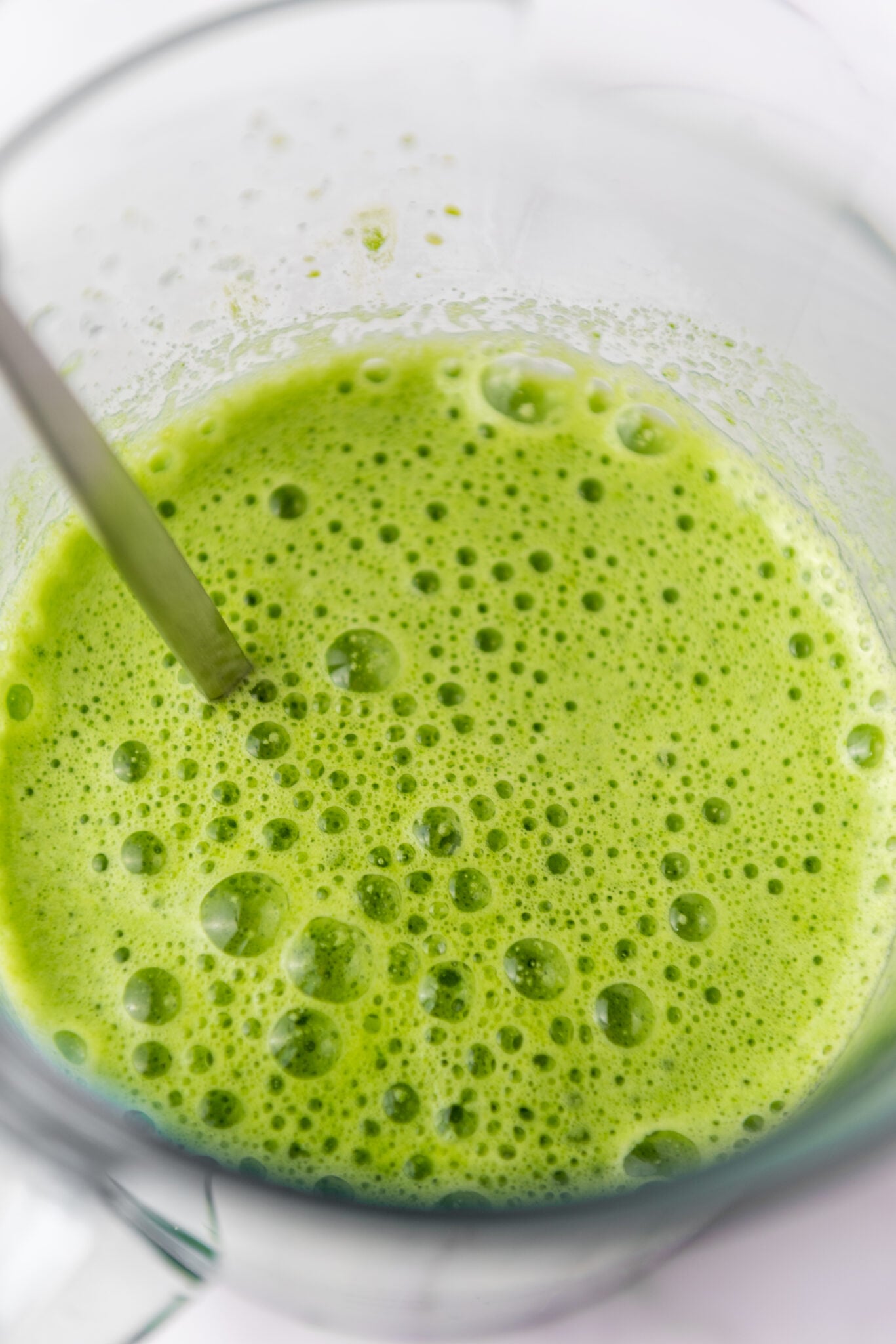 A close-up shot of the glass, showcasing the green juice's vibrant color and texture, with tiny bubbles from the fresh extraction