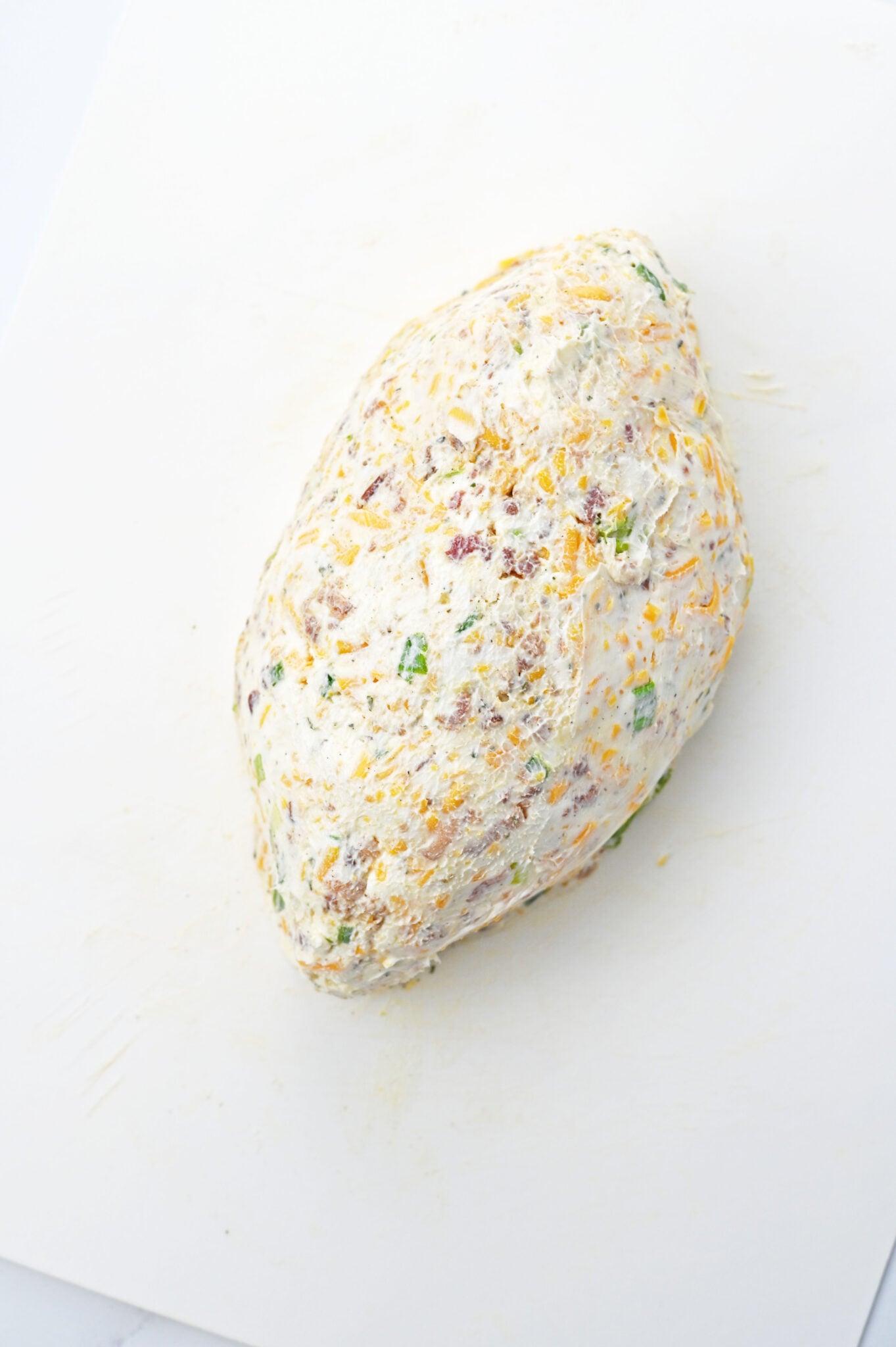 Shaping the Cheeseball: Hands molding the cheese mixture into a football shape on a parchment-lined tray.