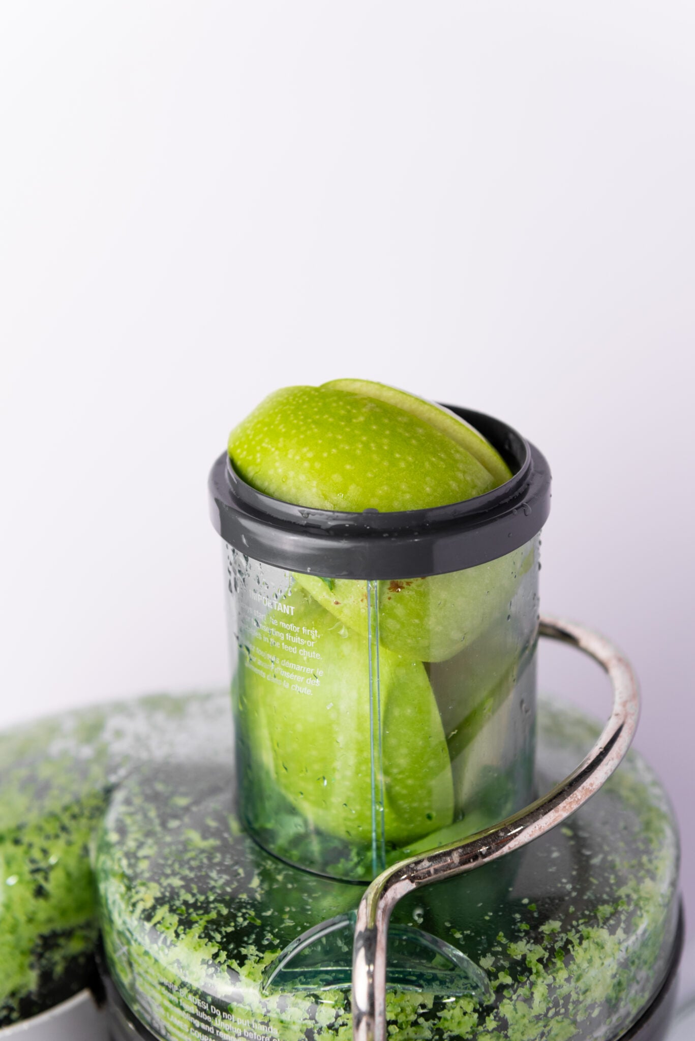 Top-down perspective of a Granny Smith apple, freshly cut and cored, being added into the juicer.