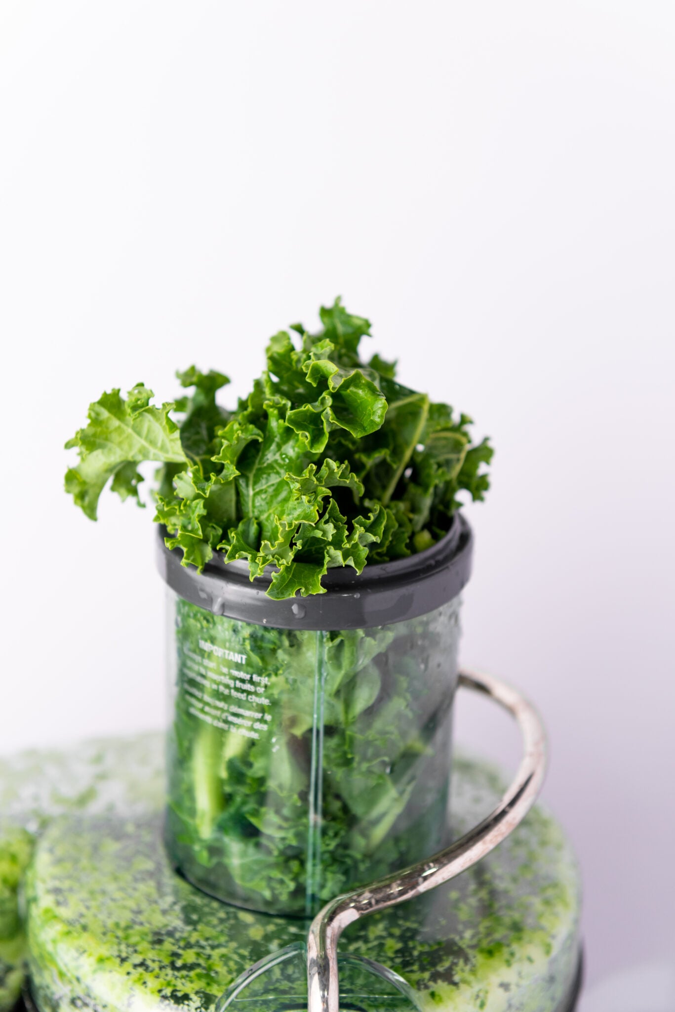 Overhead view of fresh kale being fed into the juicer with its vibrant green leaves contrasting the metallic surface of the juicer.
